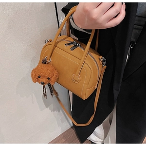 Détail du sac bowling en cuir avec un joli charm de chien en peluche marron sur l'anse