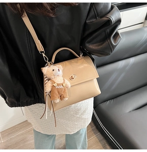 Detail view of beige retro crossbody bag with golden clasp and cute bear charm pendant