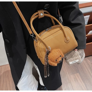 Détail du sac à main en cuir marron avec double fermeture éclair et breloque peluche chien