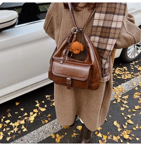 Sac à dos en cuir marron avec breloque ours présenté dans un décor de rue automnal