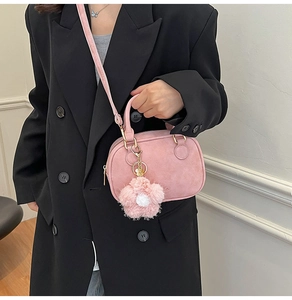 Detail of a light pink suede mini crossbody bag featuring a round handle and floral charm
