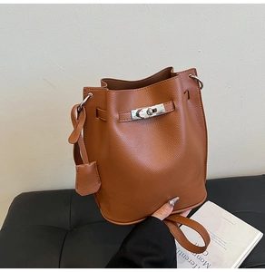 Close-up of brown lychee grain leather bucket bag with silver metal rotating lock and tag