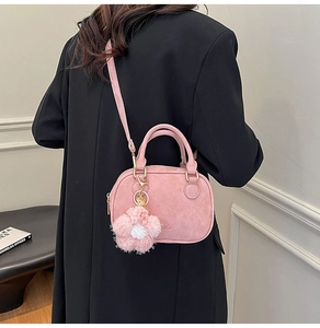 Pink suede pillow bag with plush flower pendant shown on a black wool coat