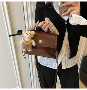 Detalle de bolso de cuero brillante marrón oscuro con colgante de oso y hebilla metálica