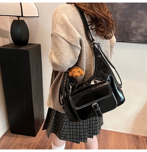 Détail du sac hobo noir brillant avec coutures blanches et breloque ours