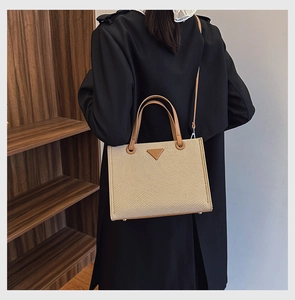Detail of straw tote bag featuring brown leather trim and detachable shoulder strap