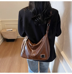 Brown leather hobo bag with a black and white checkered scarf detail and metal logo