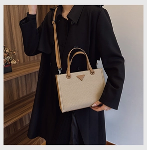 Close-up of beige woven tote bag with brown leather handles and triangle patch detail