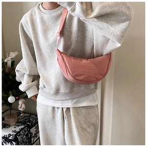 Pink nylon crescent crossbody bag worn with a casual gray outfit in a cozy home setting
