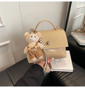 Detalle del bolso beige de charol con cierre giratorio y accesorio decorativo de osito