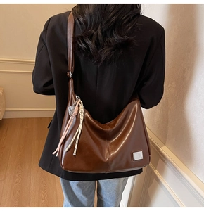 Brown leather tote bag featuring a pink woven tassel and silver metal brand plate