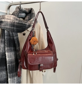 Détail du sac hobo en cuir verni bordeaux avec breloque peluche sur tenue d'automne