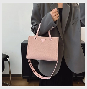 Detail of the light pink textured tote bag with double handles and a stylish crossbody strap