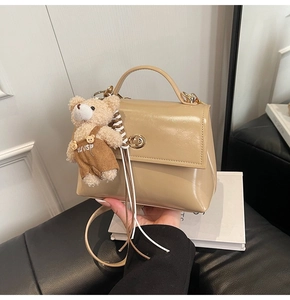 Detalle del bolso de charol caqui claro con cierre dorado y colgante de oso pequeño