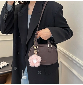 Close-up of a dark brown crossbody bag with a pink plush flower charm and gold hardware