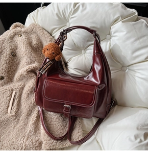 Détail d'un cabas bordeaux avec boucle argentée et pendentif chiot en peluche sur fond blanc