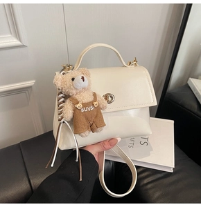 Detalle del bolso crema con cierre giratorio de metal y accesorio de amuleto de oso de peluche