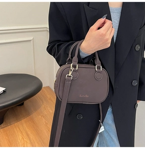 Detail of a dark brown leather crossbody pillow bag with gold hardware and brand logo