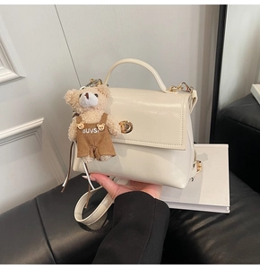 Detalle de bolso de cuero blanco crema con cierre dorado y colgante de oso de peluche