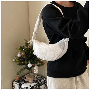 Detail of white nylon crescent bag with crinkled texture worn by a model in cozy room