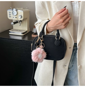 Detail of a chic black satchel with gold hardware and floral charm on a white blazer