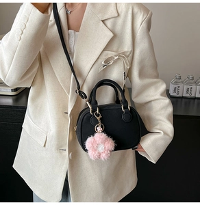 Detail of black mini Boston bag with pink floral charm on a white blazer model