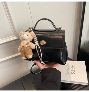 Detalle del bolso de cuero negro con cierre dorado y un colgante de oso de peluche