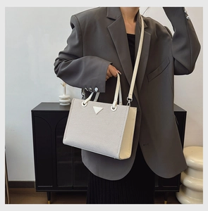 Detail of white woven tote bag with a triangle logo plaque and detachable leather strap