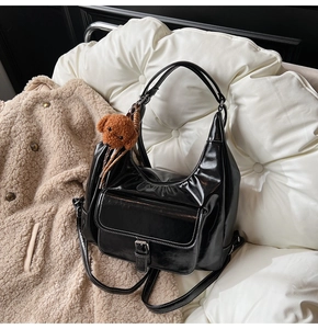 Détail d'un sac cabas noir brillant avec poche avant à boucle et charme d'ours brun