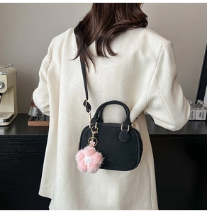 Detail of black leather satchel with pink floral charm and gold hardware strap
