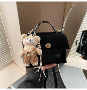 Close-up of black patent leather handbag with gold lock and plush bear pendant