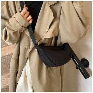 Close-up of black nylon crescent crossbody bag worn with a beige trench coat