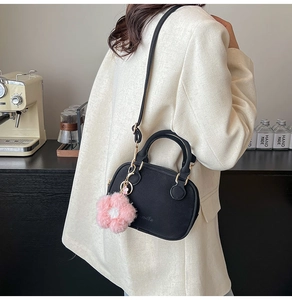 Close-up of black mini boston bag with golden zipper and pink plush flower charm