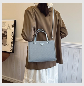 Detail view of light blue woven tote bag with iconic triangle patch and adjustable strap