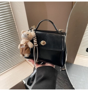 Detailed view of black square handbag featuring golden twist lock and a cute bear pendant