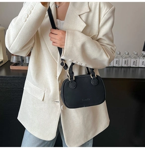 Detail of black mini crossbody bag with top handle worn on a casual cream blazer