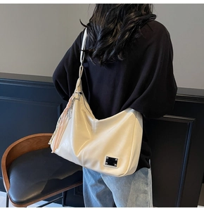 Detail of off-white leather hobo bag with pink tassel charm and metal logo plate