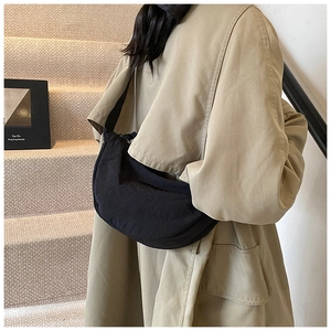 Detail of black crescent nylon crossbody bag worn with a khaki trench coat