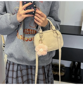 Detail of a beige top handle bag featuring a pink floral charm and metal logo accent
