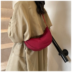 Red nylon crescent bag styled over a khaki trench coat in a modern minimalist setting