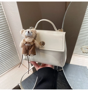 Detail of white glossy leather handbag with a metal twist lock and a cute plush bear charm