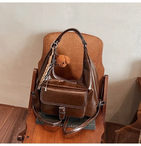 Détail d'un sac cabas en cuir marron avec charme d'ours en peluche et pompon sur chaise