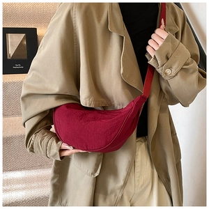 Detail view of dark red nylon crescent crossbody bag worn with a stylish beige trench coat
