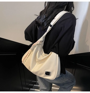 Close-up of ivory large tote bag featuring woven tassel detail and metal tag