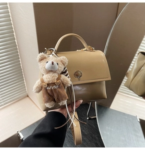 Detail view of khaki rectangular handbag with gold twist lock and plush bear pendant