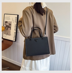 Rear view of a model wearing a black woven tote bag with silver hardware and shoulder strap