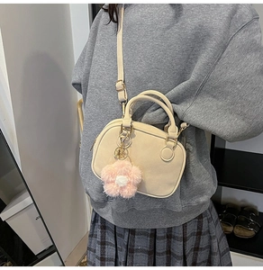 Close-up of a beige fashion handbag with pink floral charm and gold-toned metal hardware