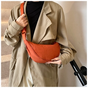 Burnt orange nylon crescent crossbody bag styled with a classic beige trench coat