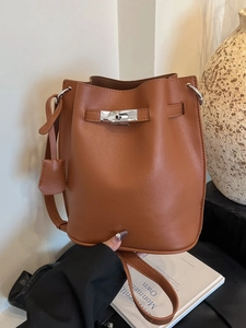Chic brown lychee leather bucket bag with silver twist lock shown in a stylish hand-held pose