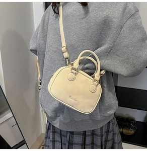 Detail shot of a cream beige crossbody pillow bag with metal logo and shoulder strap